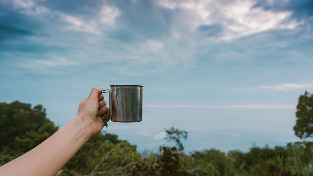 persona sosteniendo una taza hacia el cielo