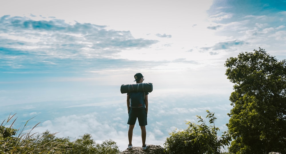 Mann im schwarzen Hemd steht auf Klippe mit Blick auf Wolkenmeer