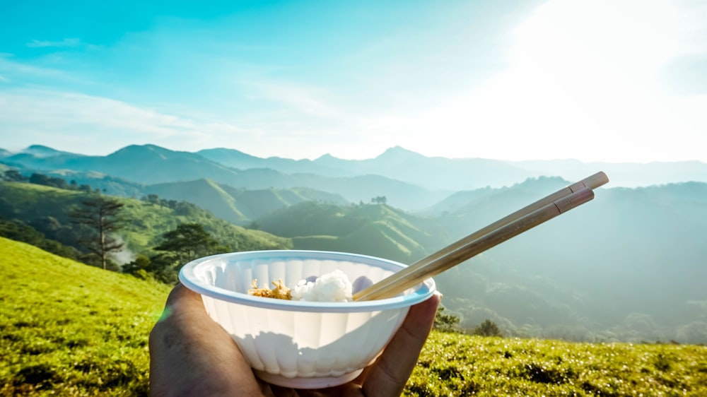 person holding bowl of rice with chopsticks