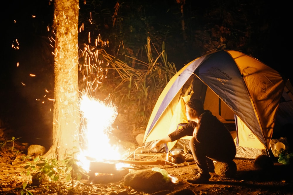 man cooking beside dome tent taken at nighttime