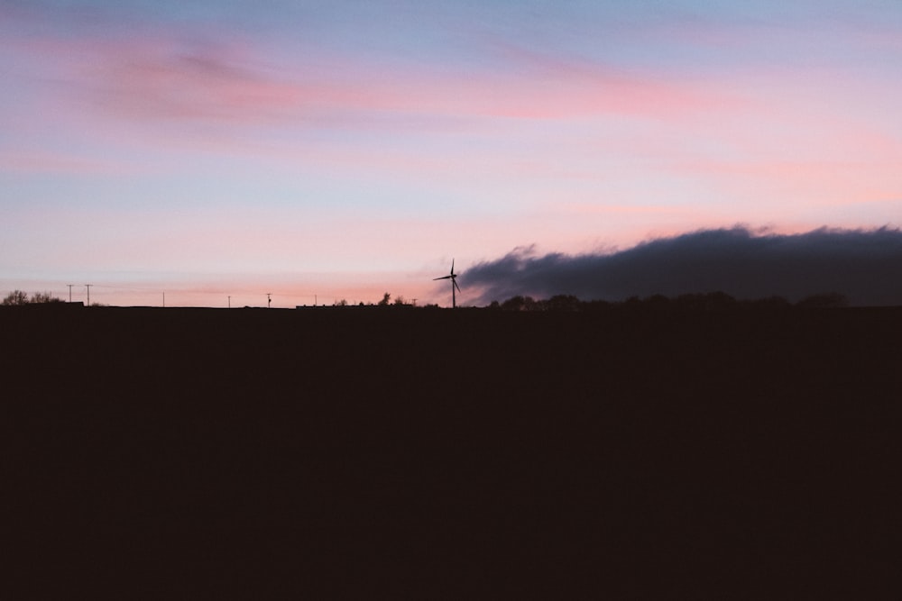 a pink and blue sky with a wind turbine in the distance