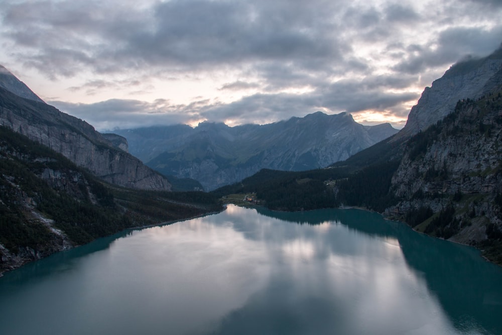 calm body of water between mountains under white clouds and blue sky