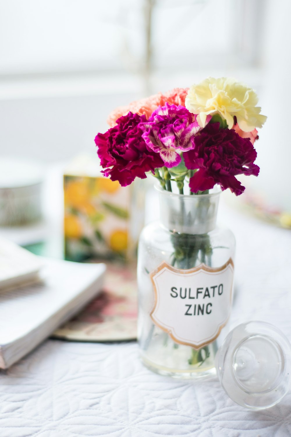 pink, red, and yellow flower arrangement in clear glass vase near white book