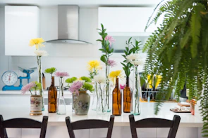 A creator arranging fresh plants on a warm cream kitchen countertop with slate-accented cabinetry in the background.