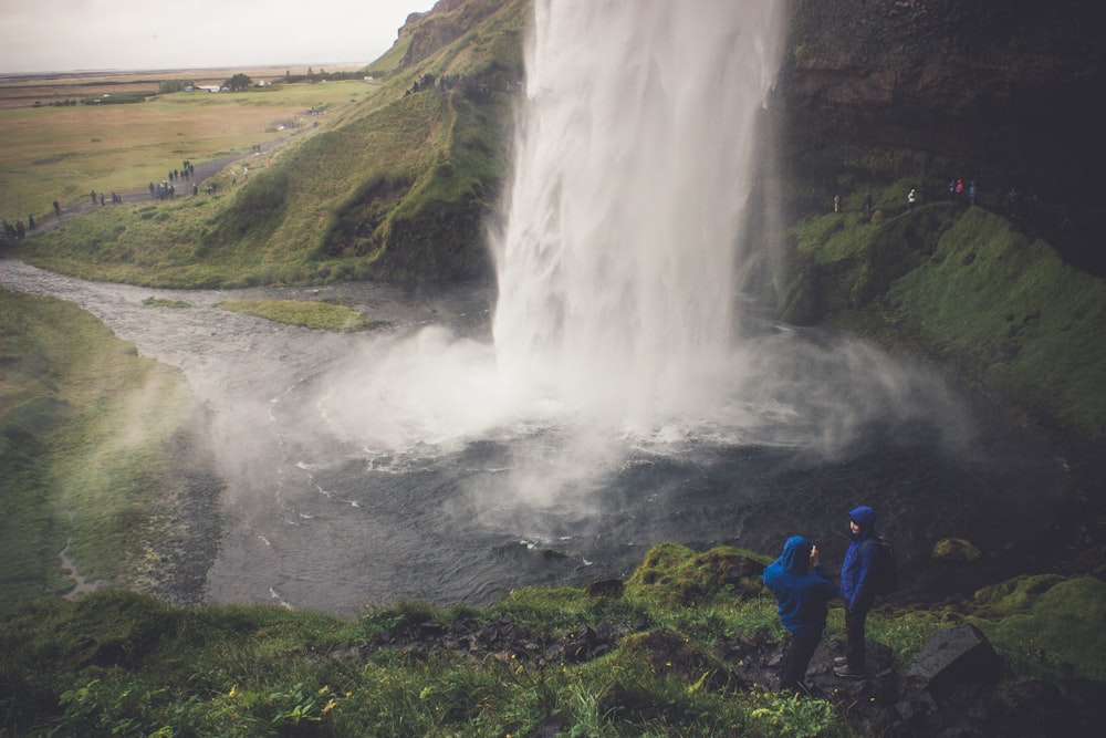 two person wearing blue hoodie standing on ground in front of waterfalls