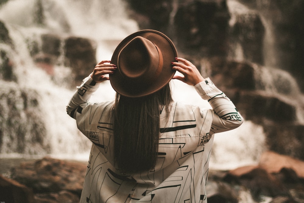 Fotografia de foco seletivo da mulher segurando o chapéu marrom Fedora durante o dia