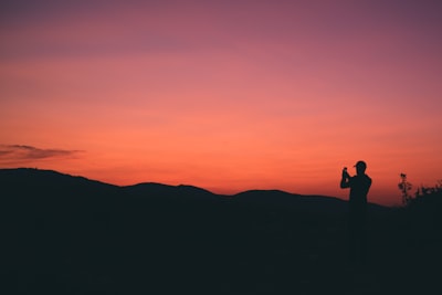 silhouette of person taking photo of mountain during sunset kosovo teams background