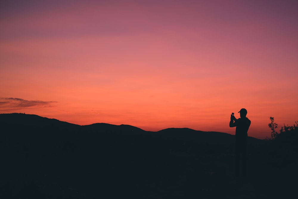 silhouette of person taking photo of mountain during sunset