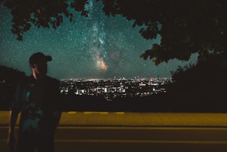A nighttime city skyline merging seamlessly with a vibrant star-filled galaxy above.