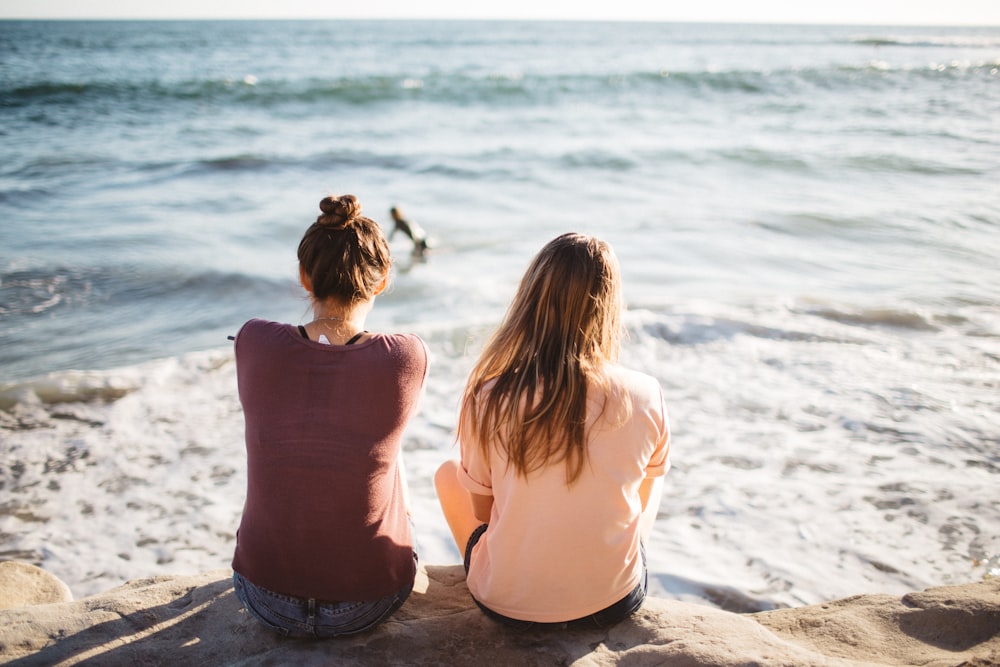 two women sitting on cliff looking at the ocean