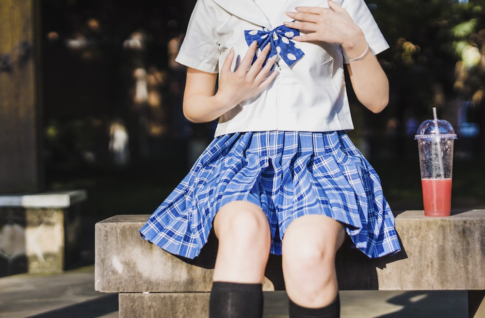 person in white and blue school uniform seating on beach with cup