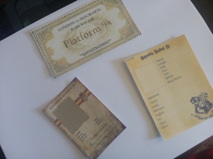 A collection of themed cards is arranged on a flat surface. There is a decorative ticket marked 'Platform 9 3/4' indicating a fictional journey to Hogwarts. Two student ID cards with Hogwarts branding are placed nearby, both featuring forms to fill out personal details.
