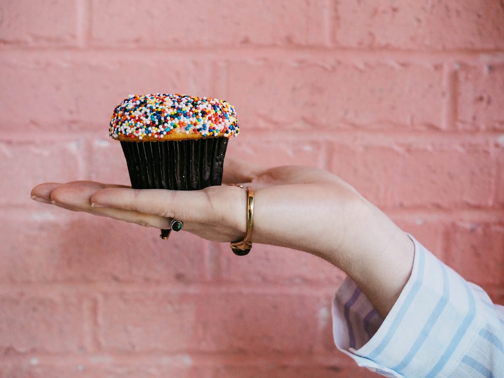 una persona che tiene un cupcake con spruzzate su di esso