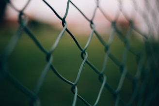 Close-up of thick aluminum fence clips securing a wire fence on a sunny farm.