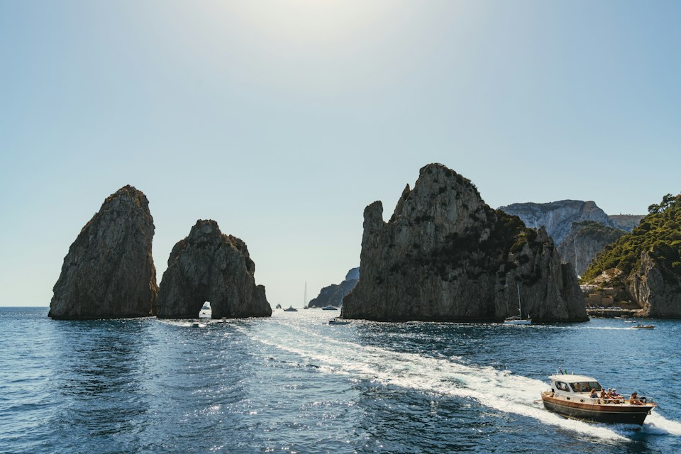A boat passing the Faraglioni sea stacks off Capri on a bright sunny day