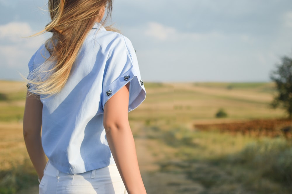 Mujer con camisa de vestir blanca de pie en el campo de hierba verde durante el día