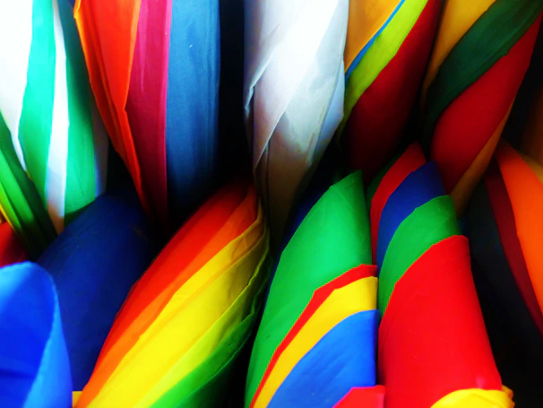 A row of foldable umbrellas in various bright colors displayed on a wooden table.