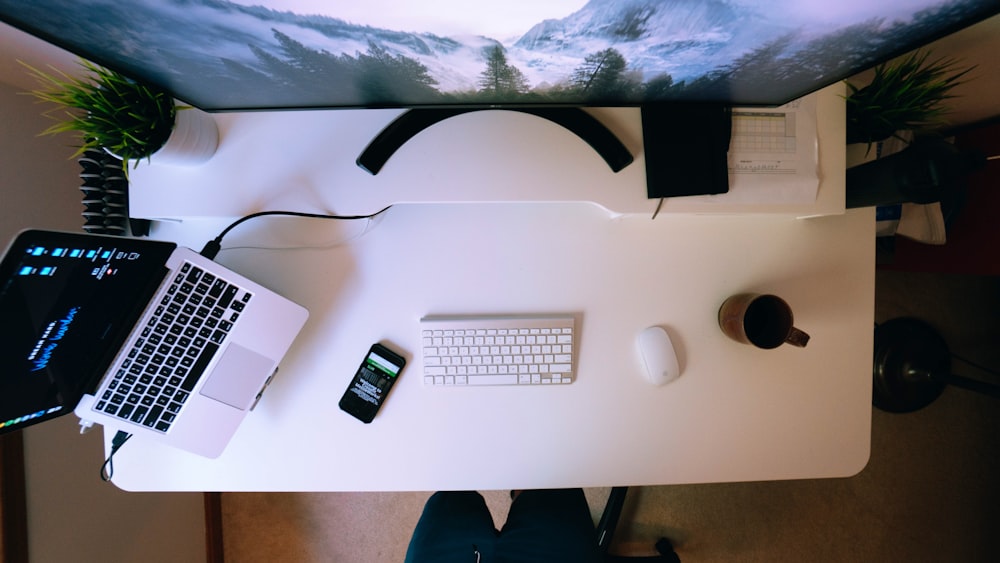 스마트폰 근처에서 노트북을 켰고 흰색 컴퓨터 책상 위에 Apple 키보드와 Magic Mouse를 켰습니다.