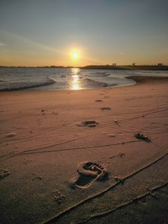 A serene beach scene with gentle waves and footprints in the sand at sunset