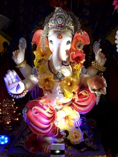A beautifully decorated statue of Lord Ganesha adorned with vibrant flowers and intricate jewelry. The statue features detailed craftsmanship with vibrant colors and a serene expression.