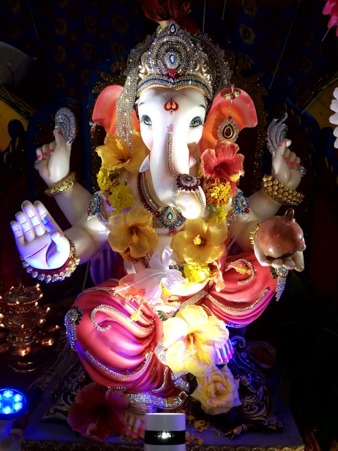 A beautifully decorated statue of Lord Ganesha adorned with vibrant flowers and intricate jewelry. The statue features detailed craftsmanship with vibrant colors and a serene expression.