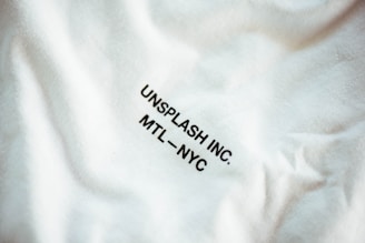 A close-up view of a fabric with slight wrinkling and printed text reading 'UNSPLASH INC. MTL - NYC' in black uppercase letters.