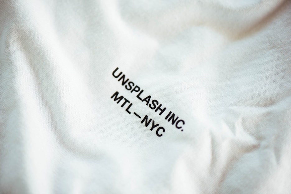 A close-up view of a fabric with slight wrinkling and printed text reading 'UNSPLASH INC. MTL - NYC' in black uppercase letters.