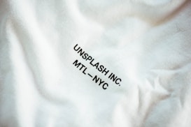 A close-up view of a fabric with slight wrinkling and printed text reading 'UNSPLASH INC. MTL - NYC' in black uppercase letters.