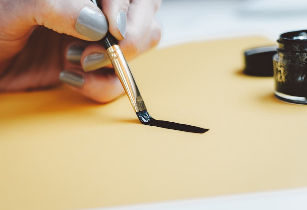 person writing on beige paper using black ink