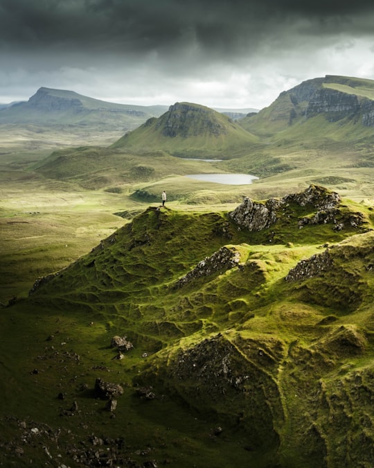 aerial view photography of person standing on mountain under cloudy sky in The Quiraing United Kingdom