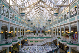 Spacious shopping mall atrium featuring large-scale artificial flower sculptures with green and gold accents.