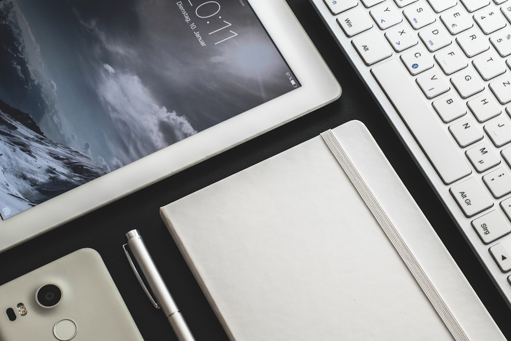 a tablet, a pen, and a notebook on a desk