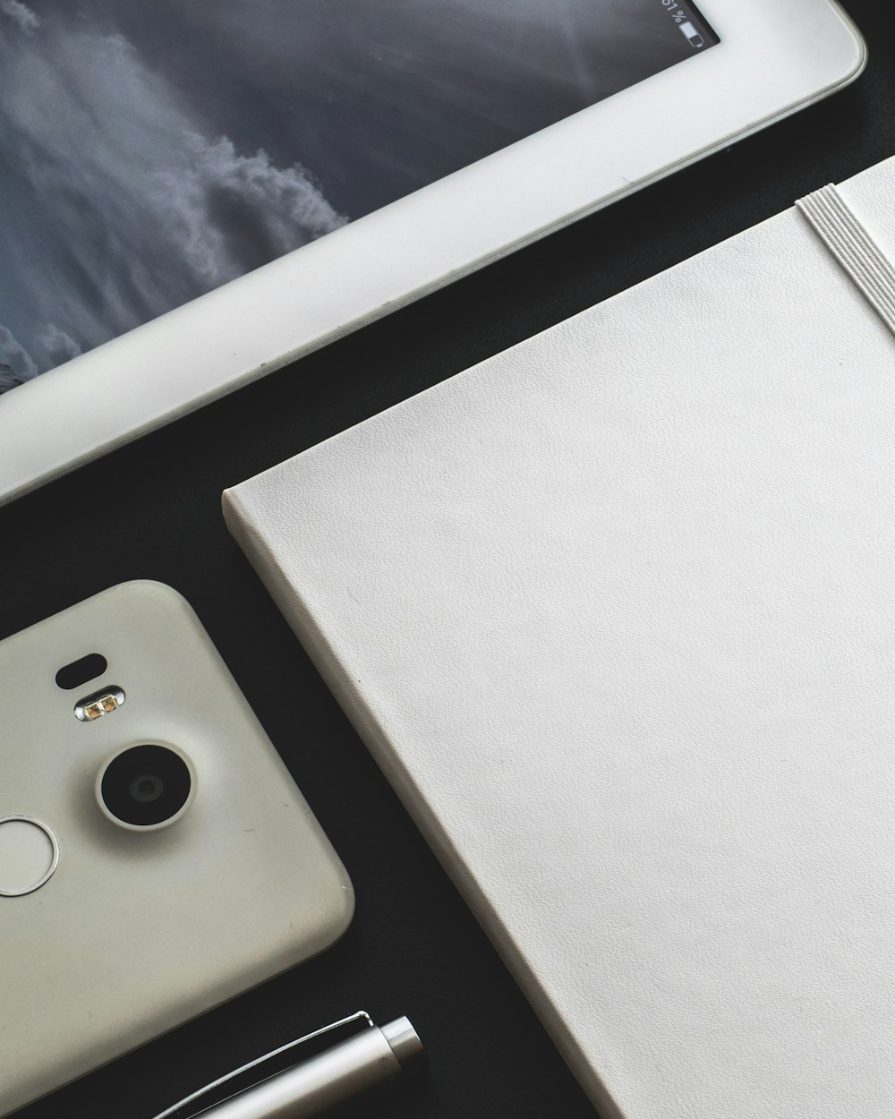 a tablet, notebook, pen, and cell phone on a table