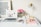A neatly arranged desk features a laptop displaying a website, a vase of pink roses, a brass desk lamp, and various office supplies. There's a framed motivational quote on the wall behind and notebooks with glasses and a smartphone on the desk.