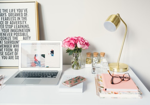 MacBook Air beside gold-colored study lamp and spiral books