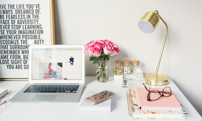 MacBook Air beside gold-colored study lamp and spiral books