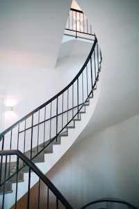 A sleek spiral metal staircase with stainless steel handrails in a bright modern home interior.