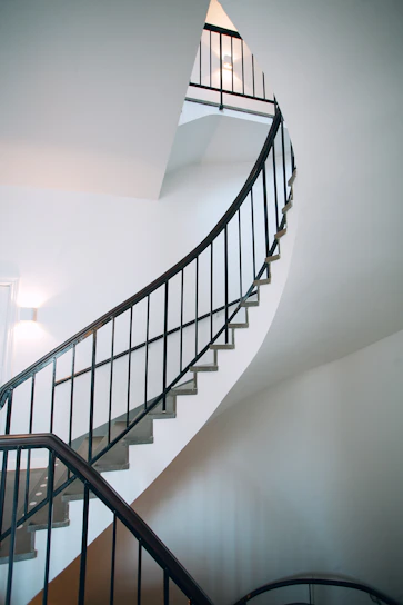 A sleek spiral metal staircase with stainless steel handrails in a bright modern home interior.