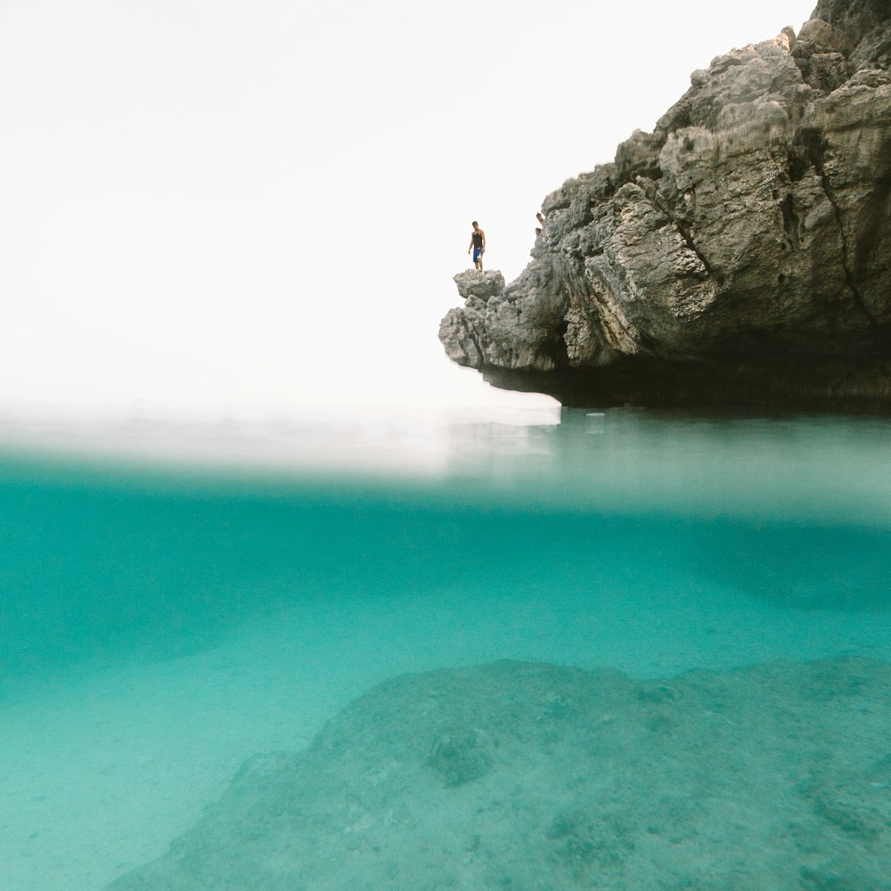 uomo in piedi sulla montagna grigia della roccia davanti allo specchio d'acqua durante il giorno