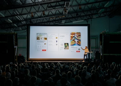 Na czym polega optymalizacja SEO strony internetowej? - person discussing while standing in front of a large screen in front of people inside dim-lighted room