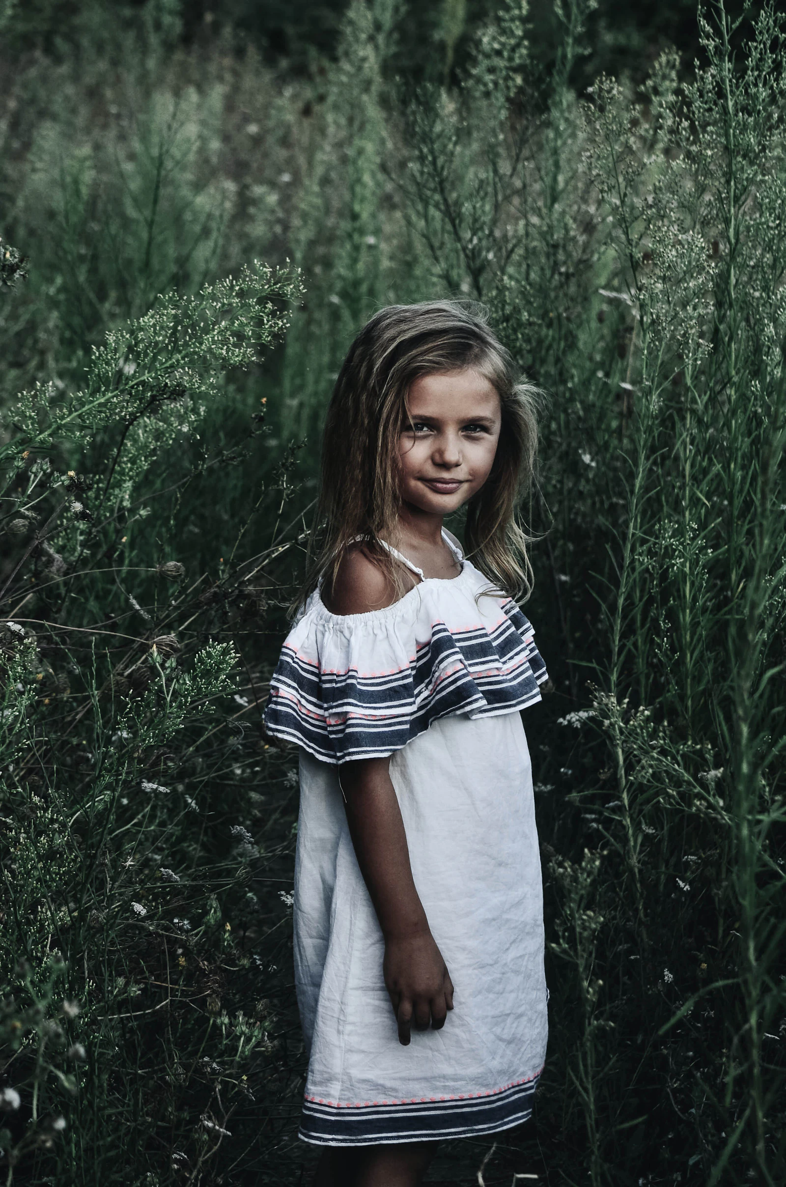 Menina de vestido branco entre gramíneas