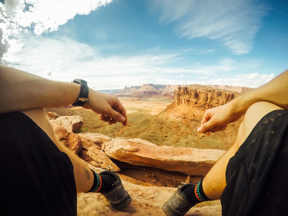 man sitting on cliff near mountains during daytime