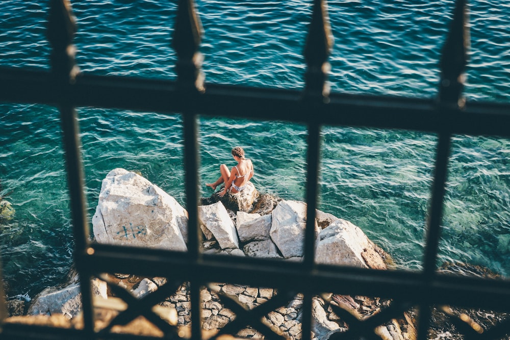 woman sitting on brown rock fragments beside body of water