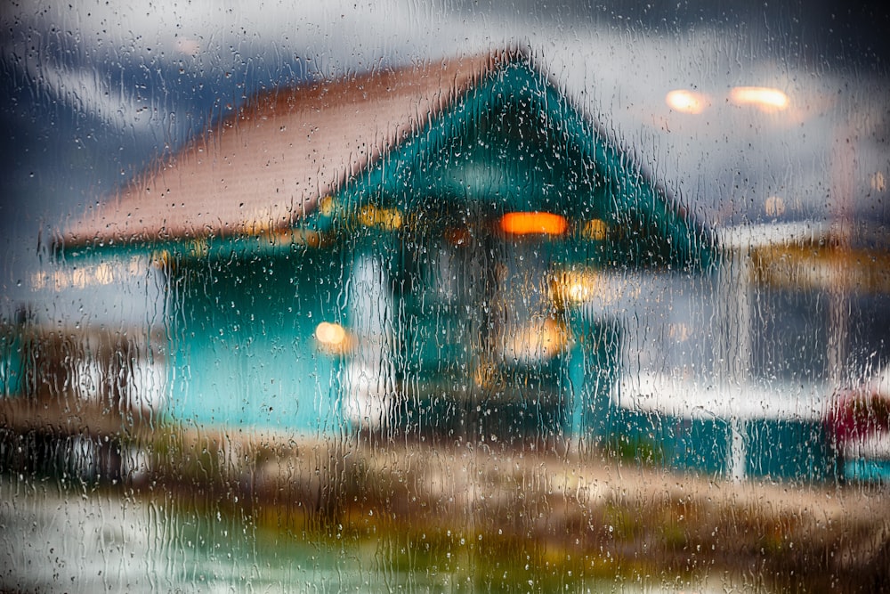 window glass filled with water drops and a view of teal wooden house