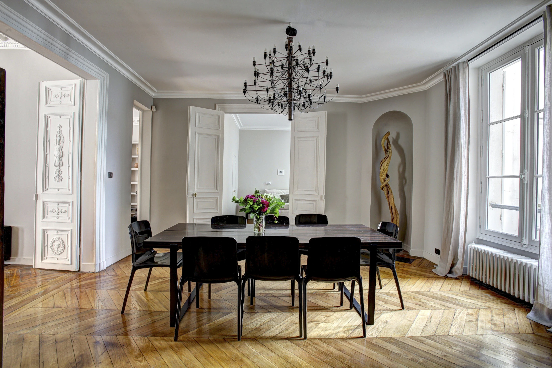 Séjour d’un appartement parisien réhabilité : moulures conservées, parquet chevron, fenêtres toute hauteur