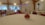 An elegantly decorated event hall with round tables covered in white tablecloths and red accents, such as chair bows and floral table centerpieces. The room has draped curtains and wooden beams, with stage lighting in the background.