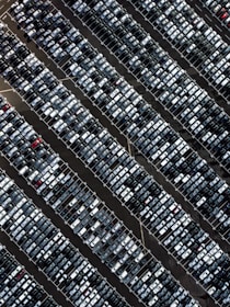 Aerial view of cars lined up in a modern parking lot with sunlight highlighting various models.
