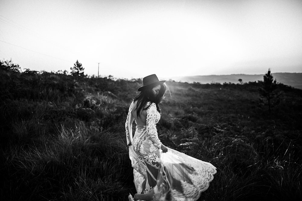 Photo en niveaux de gris d’une femme en robe debout sur un champ d’herbe