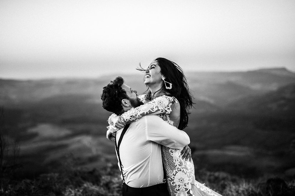 grayscale photography of man and woman hugging near hill