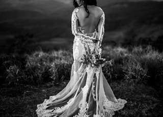 grayscale photo of woman wearing wedding dress holding bouquet of flower